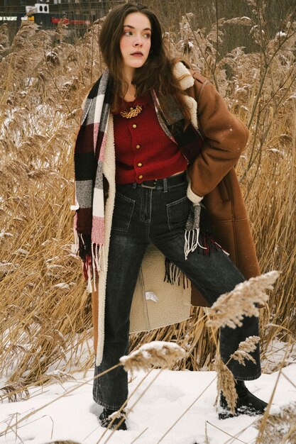 A woman showcasing a winter capsule wardrobe with neutral-colored sweaters, dark jeans, versatile boots, and a long coat. The image highlights the mix-and-match potential of each item.
