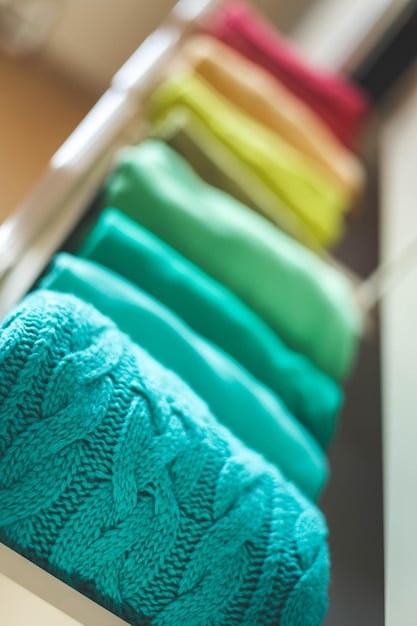 A close-up shot of a well-organized closet, focusing on details such as neatly folded sweaters, hanging blouses, and a selection of shoes. The color scheme is primarily neutral, with pops of color from accessories.