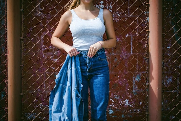 A street style photograph of a woman wearing high-waisted, cropped bell-bottom jeans with side slits, paired with a white oversized shirt and platform sandals. She is carrying a woven tote bag and wearing sunglasses.