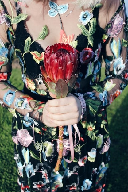 A woman wearing a dress with mixed textures and prints, including embroidered details and velvet elements. The outfit is accessorized with jewelry and statement shoes. The background is a stylish, urban street setting. The focus is on sophisticated combination of textures and attention to detail.