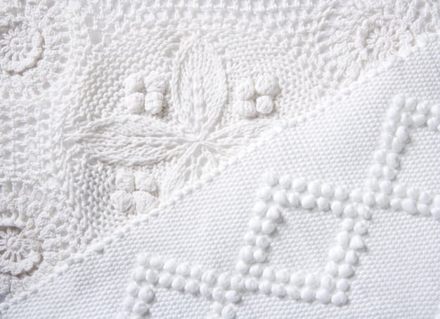 A close-up shot of different textures of white fabrics, like cotton, silk, and knitted wool, all in slightly different shades of white.