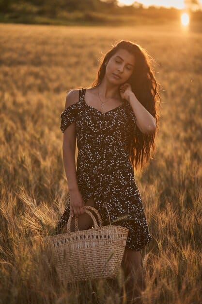 A woman with long wavy hair wearing a flowy boho dress, standing in a sunlit field. The hairstyle is natural and effortless, complementing the relaxed and earthy vibe of the dress.