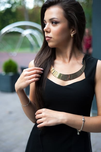 A medium shot of a woman wearing a black dress with a round neckline, paired with a bold, chunky necklace in gold. The necklace sits perfectly at the base of her neck, enhancing the neckline.