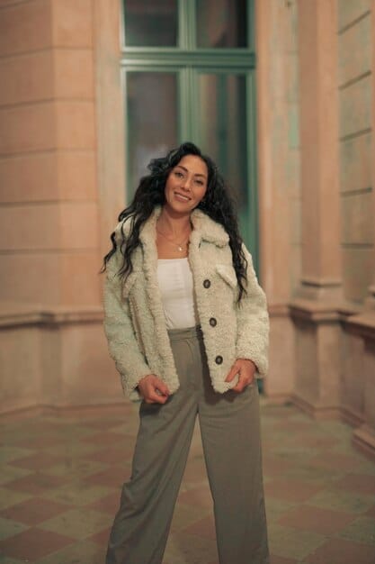 A woman wearing a versatile jacket over a casual outfit. The jacket is a neutral color, such as beige or olive, and has a simple design. She is standing in front of a backdrop of travel destinations. The jacket emphasizes the subject's adaptability to weather changes.