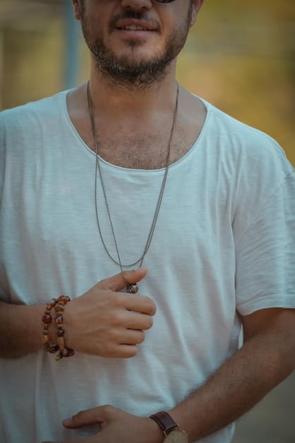 A man wearing a simple silver necklace and a leather bracelet, paired with a casual yet stylish outfit.