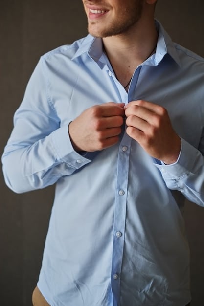 Close-up of a man's hands demonstrating the first steps of the classic shirt folding method, emphasizing the precise folding of the side and sleeve towards the center of the shirt.