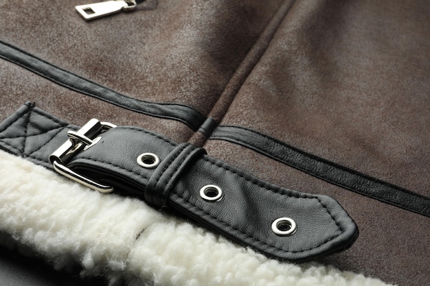 A close-up shot of a dark brown leather jacket with a slightly worn texture, showcasing its details like zippers, buttons, and stitching. The background is a blurred, neutral tone.