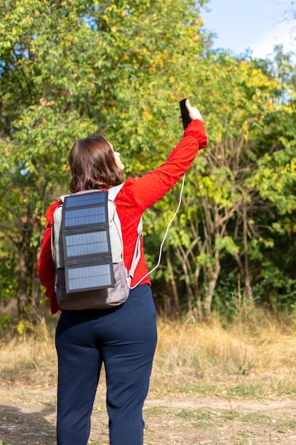 A lifestyle shot of someone using a solar-powered backpack in a sunny outdoor setting. The backpack is charging a smartphone, emphasizing the convenience and portability of solar technology for everyday use.