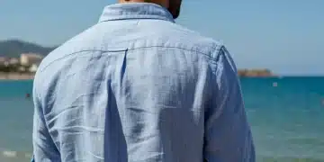 Hombre elegante con camisa de lino azul claro en una playa española soleada.