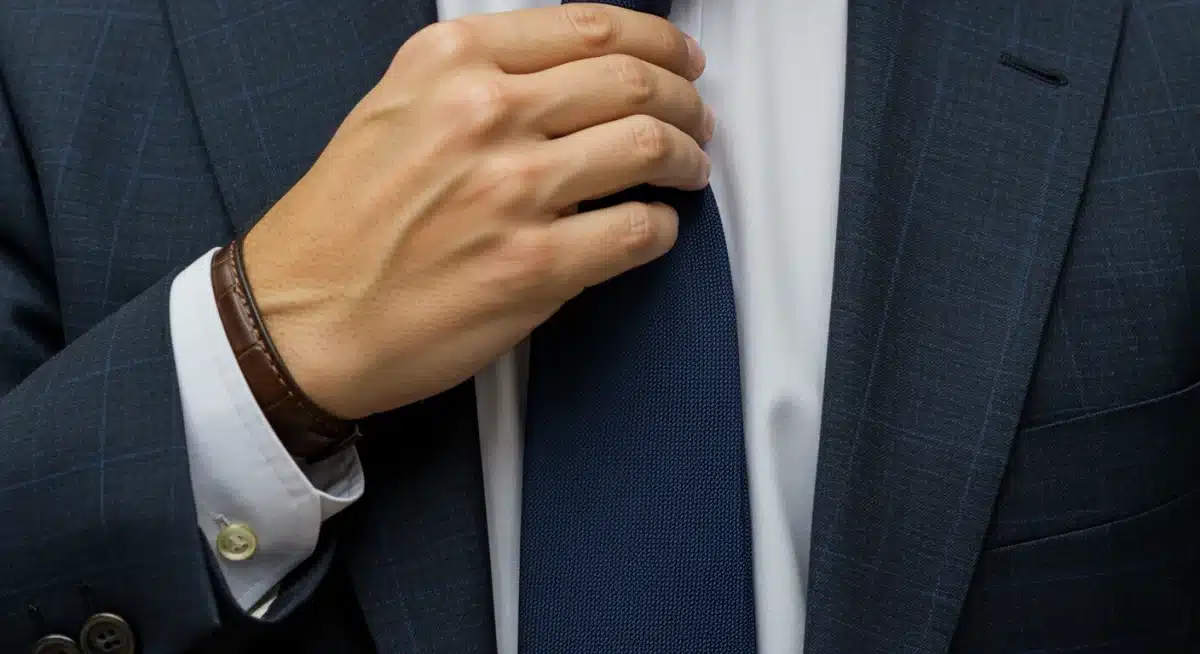 Detalle de un hombre ajustándose la corbata de un traje, mostrando elegancia y cuidado.